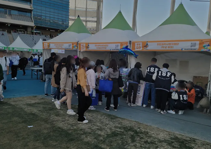 녹색 지붕 천막 부스 앞에 모인 참가자
